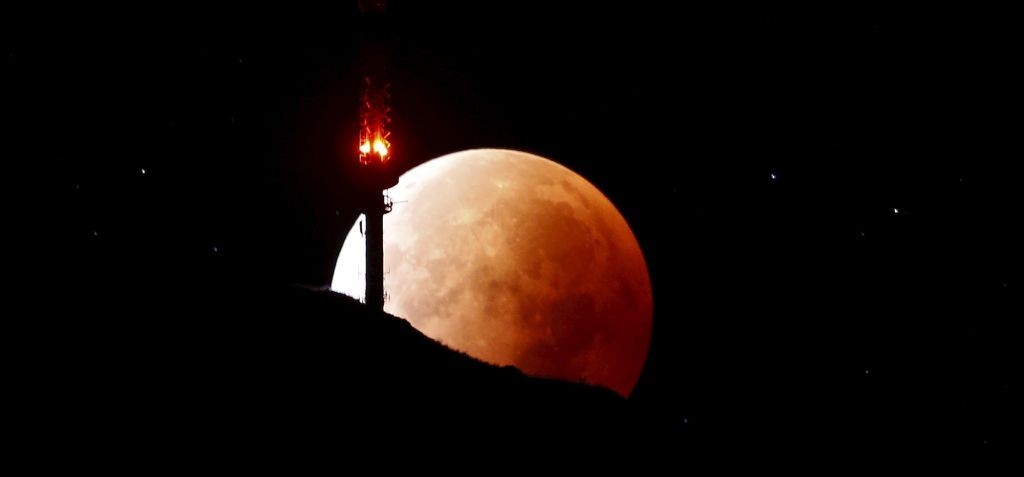 The moon, appearing in a dim red color, is covered by the Earth’s shadow during a total lunar eclipse over the peak of Mount Rigi, Switzerland, on Sept. 28